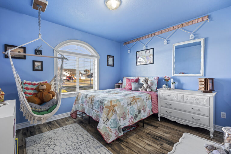A child's room with blue-painted walls, featuring a bed, swing frames, and a white desk
